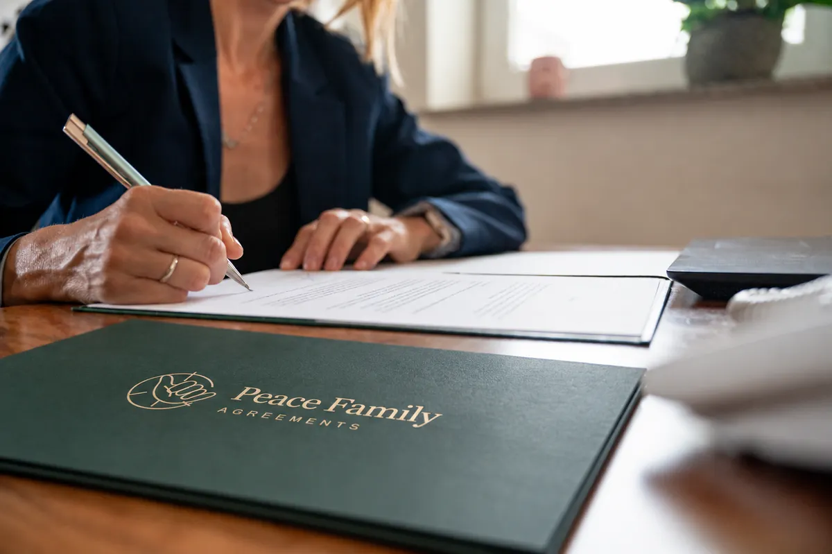 A woman signing a document beside a Peace Family Agreements folder
